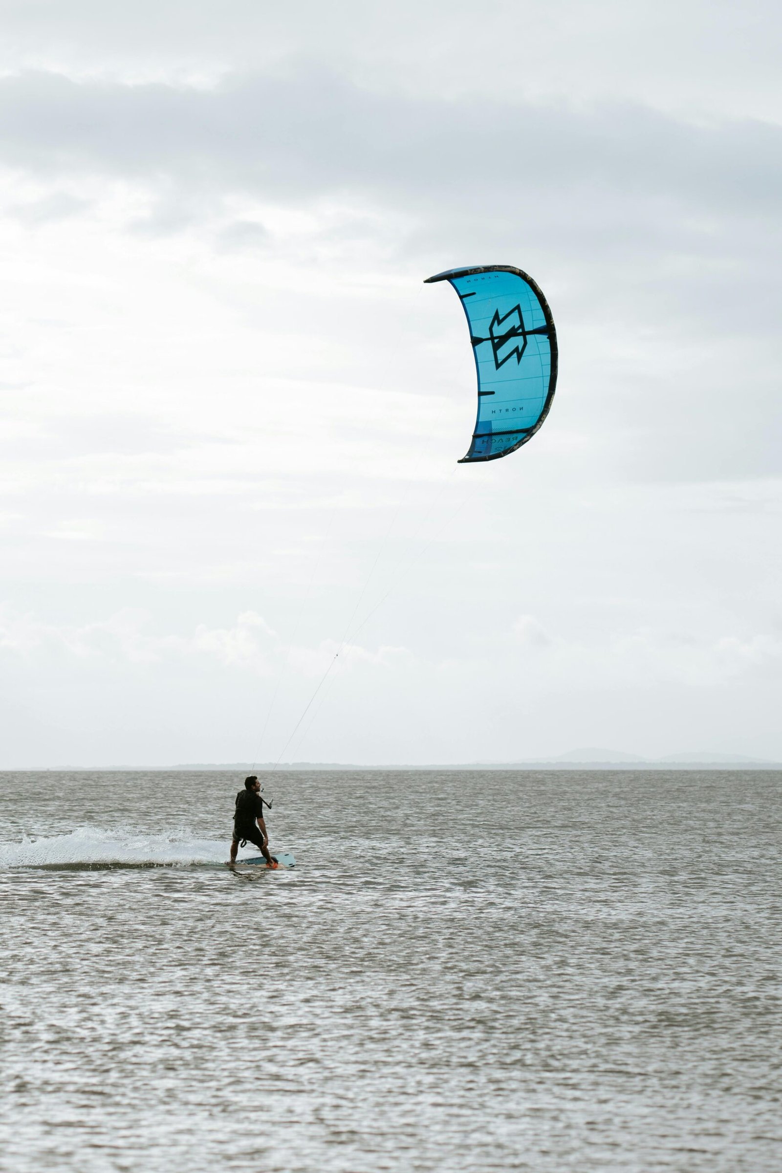 A kitesurfer rides the waves with a blue kite in Paraná, Brazil.
