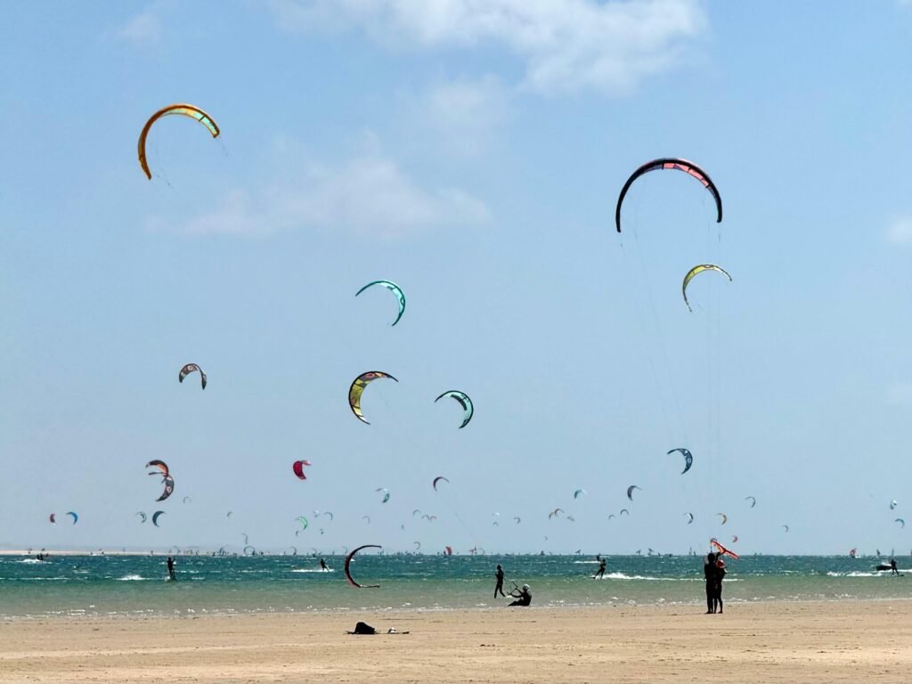 Colorful kiteboarders enjoying a sunny day at Dakhla Beach, Morocco. Vibrant kites fill the sky.